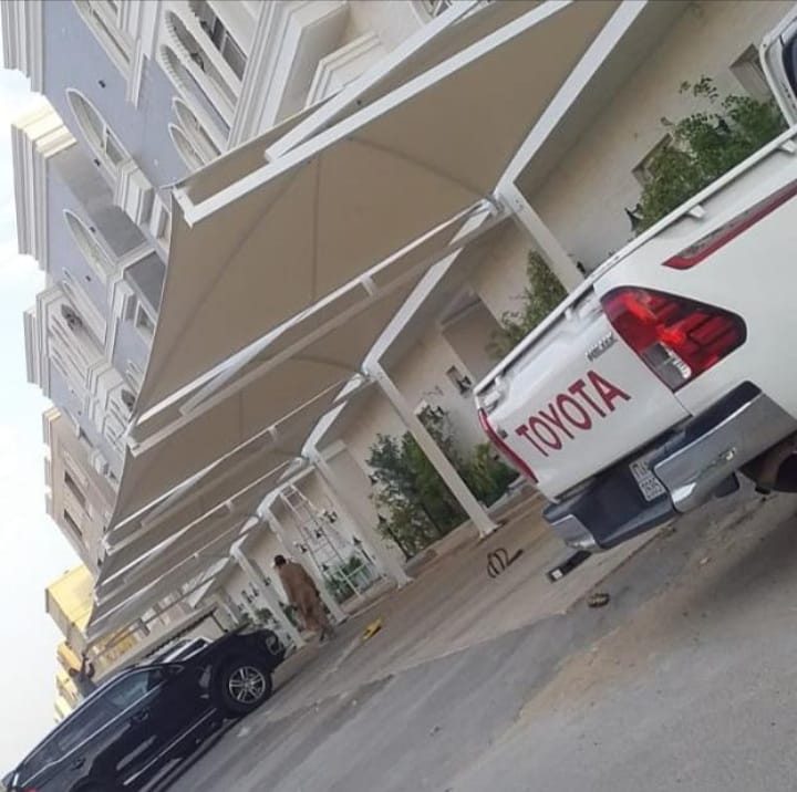 صف مظلات مواقف سيارات أمام مبنى سكني من تنفيذ عالم الظل الأول